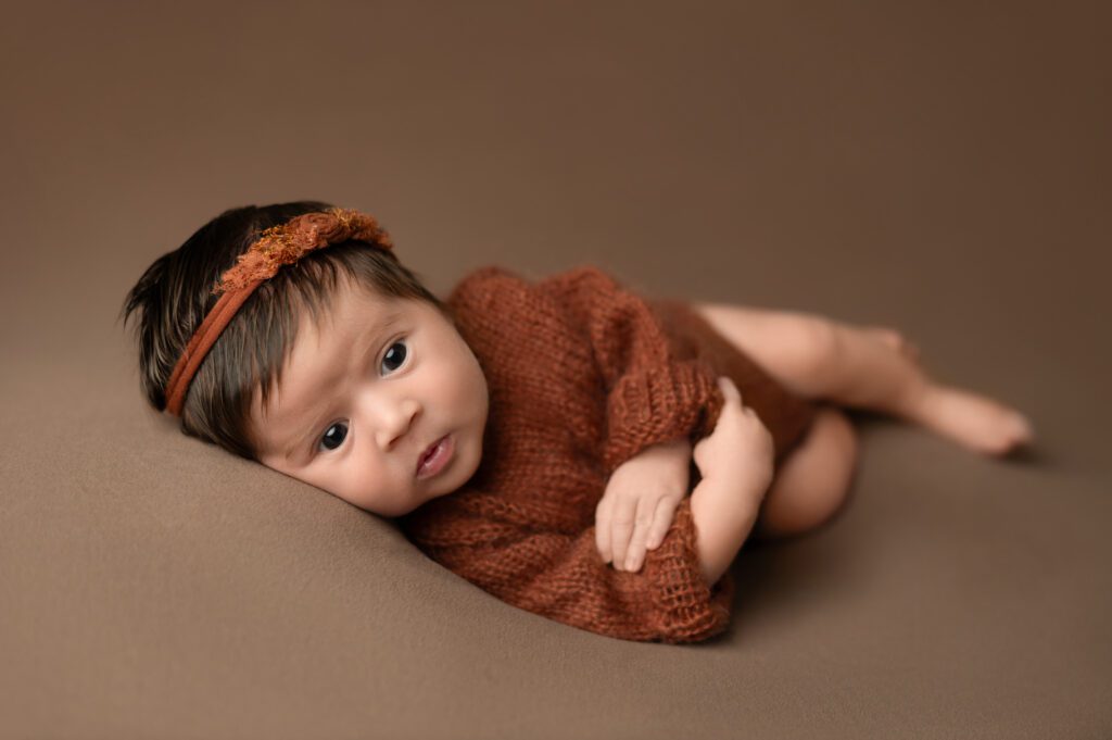 a newborn baby with dark brown clothing lying on a brown blanket
