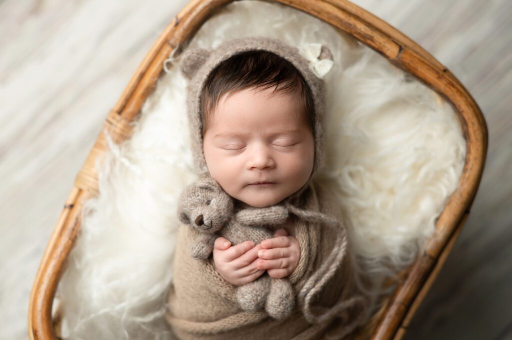 a baby sleeping with a brown blanket holding a tedy