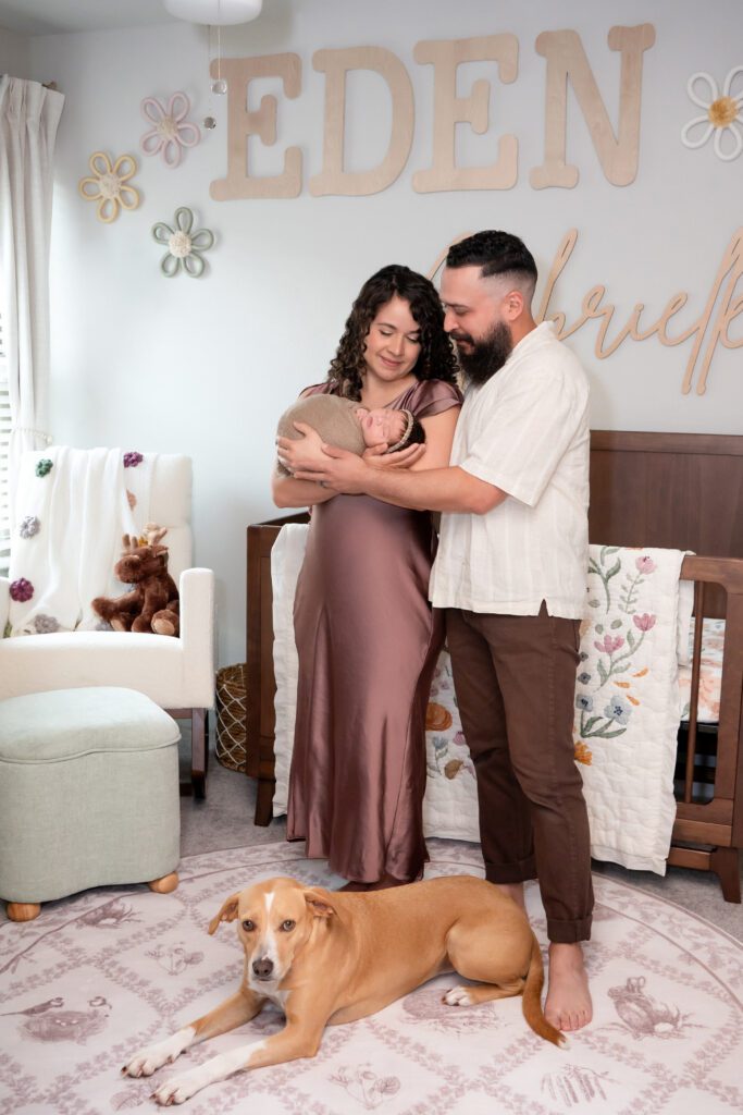 a mother and father holding a baby with a dog in home environment