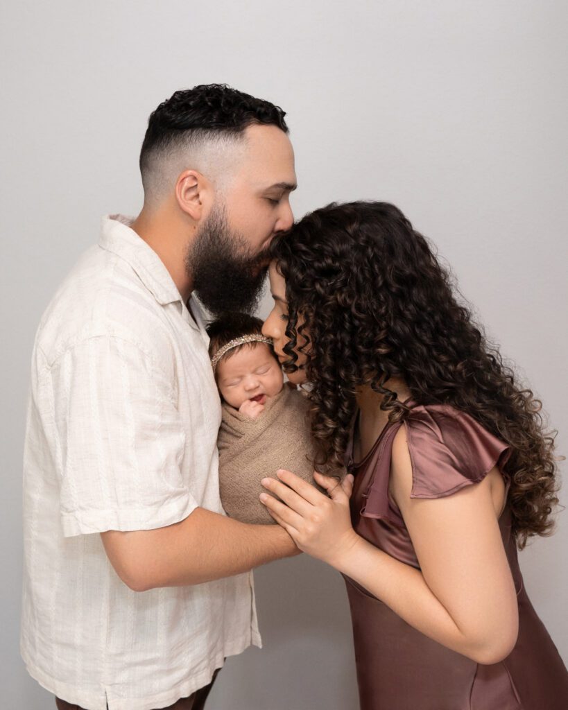 a father kissing a mother and mother kissing a baby during a newborn photoshoot